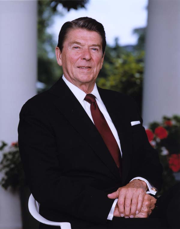 Ronald Reagan posing for a photograph outside with flowers behind him
