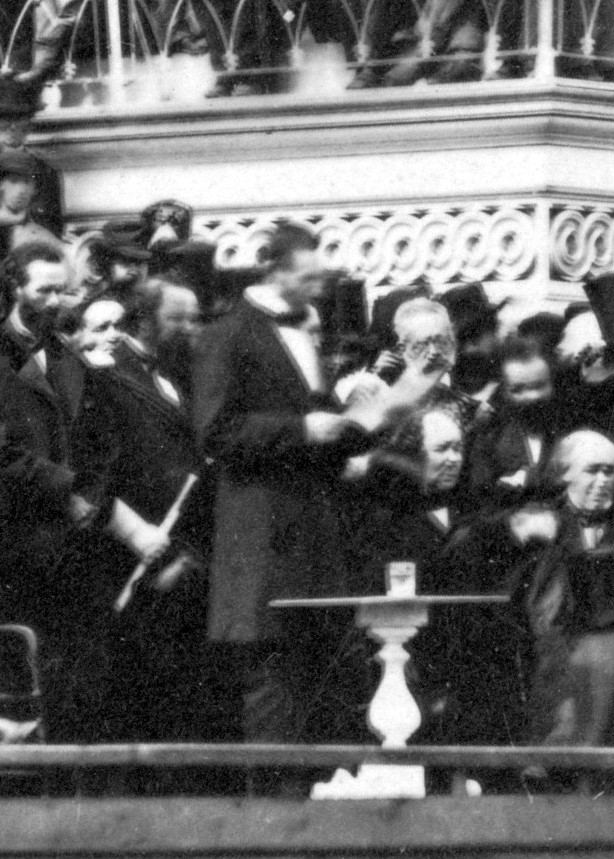 Abraham Lincoln in a suit with paper in his hand delivering his second inaugural speech.