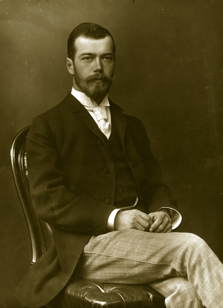An uncropped version of the previous photo, shows Nicholas II of Russia in a suit sitting on a chair and posing for a photograph at the wedding of George and Mary of the United Kingdom in 1893.