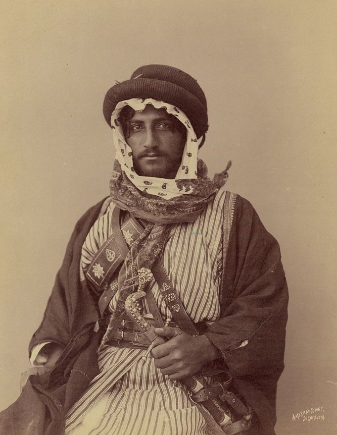 A historical photo of a bedouin warror in 1900. he is holding a weapon and wearing traditional clothing