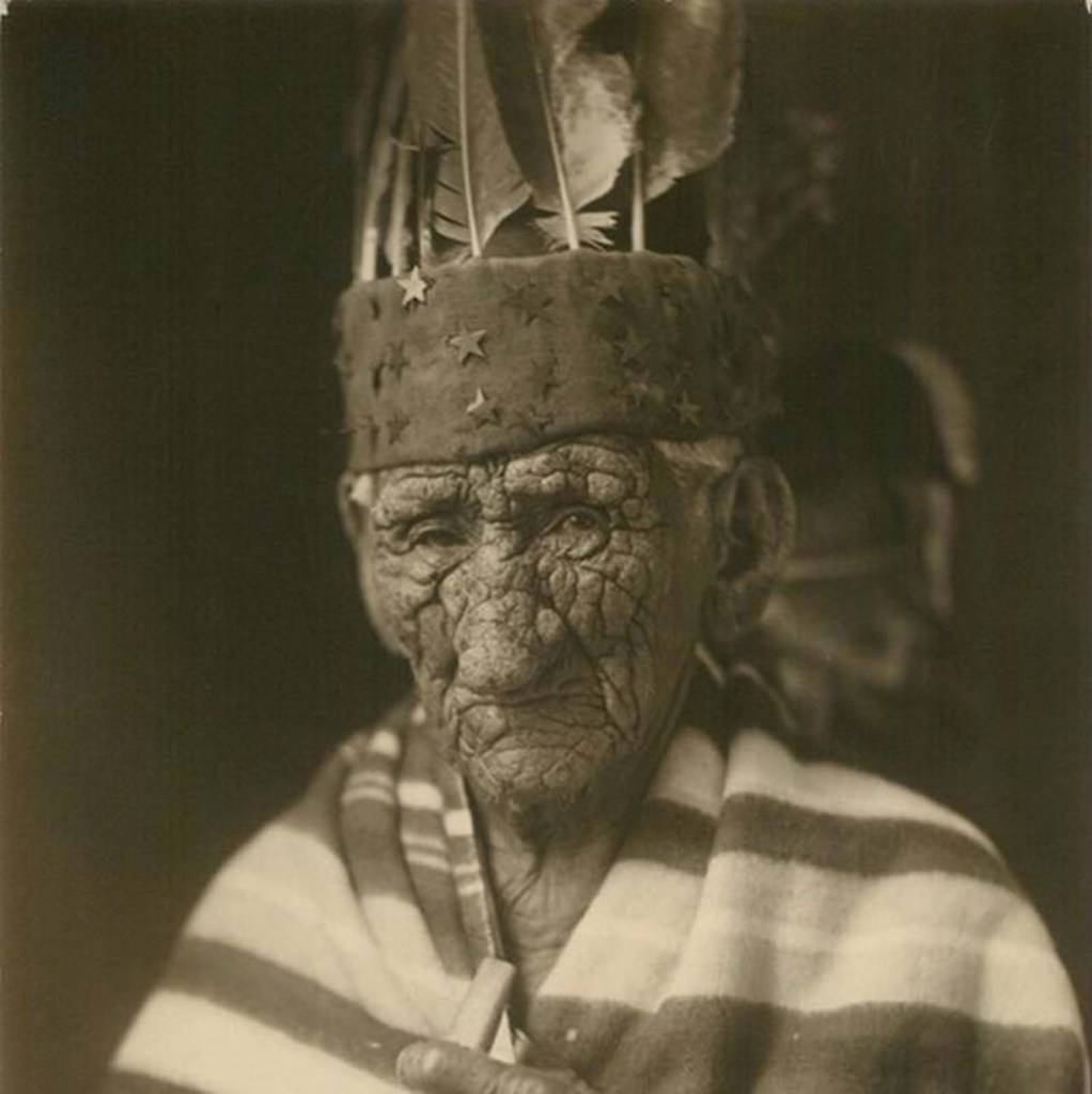 Chief John Smith with a cover wrapped around him wearing a head band covered in stars with feather coming from the top.
