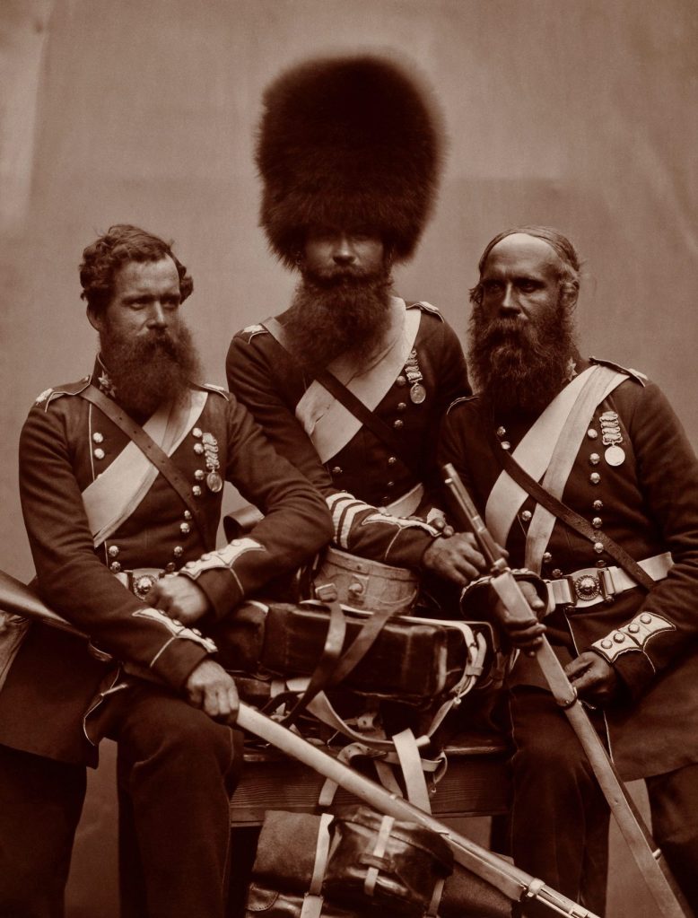 Three British army soldier in full military uniform in a photo studio along with their weapons and medals. 1856
