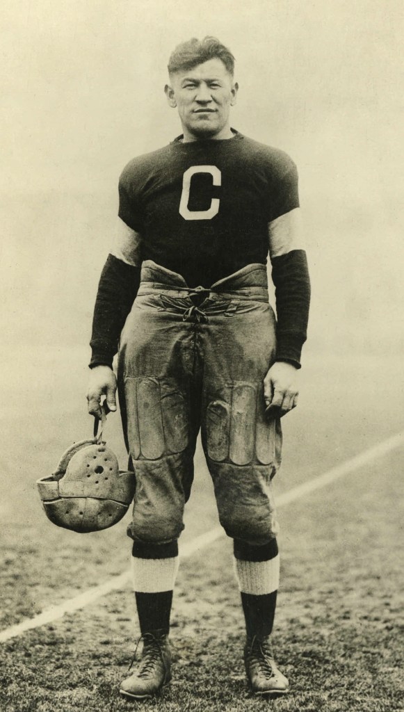 Legendary athlete, Jim Thorpe holding a helmet and wearing his Canton Bulldogs uniform in circa 1917. He is looking directly at the camera and has a big "C" on his chest.