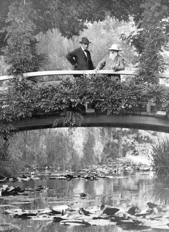 Photo of Monet standing on a bridge in his garden while showing a visitor around in 1922