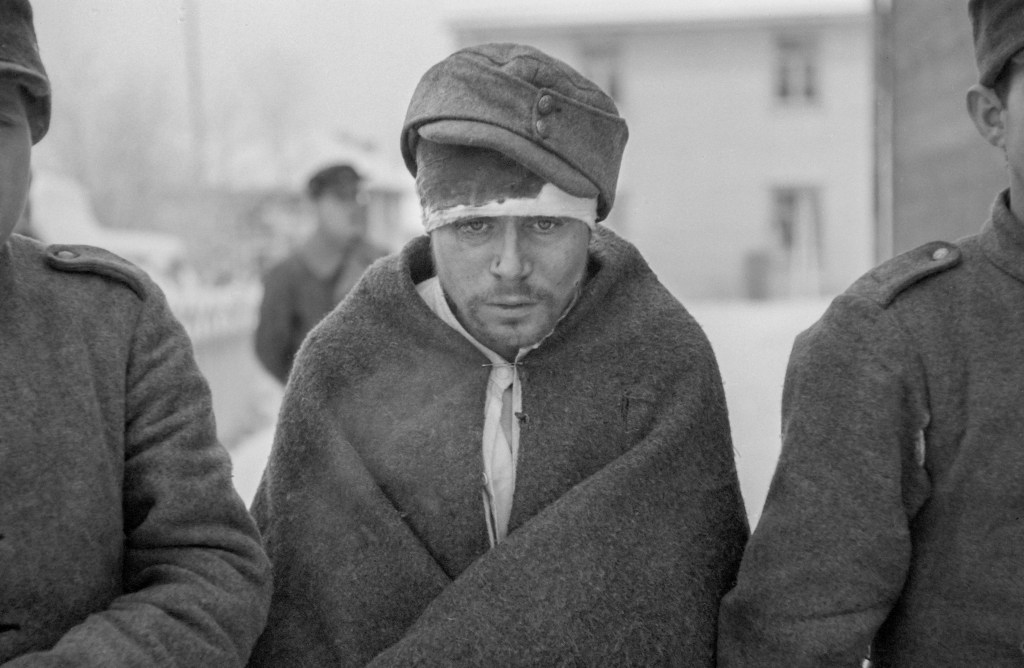An injured Prisoner of War from the Soviet Union with a bandage around his bloody head, with clothing wrapped around his body. He looks cold as he is near the Arctic Circle where temperatures can get to -43 degrees Celsius 