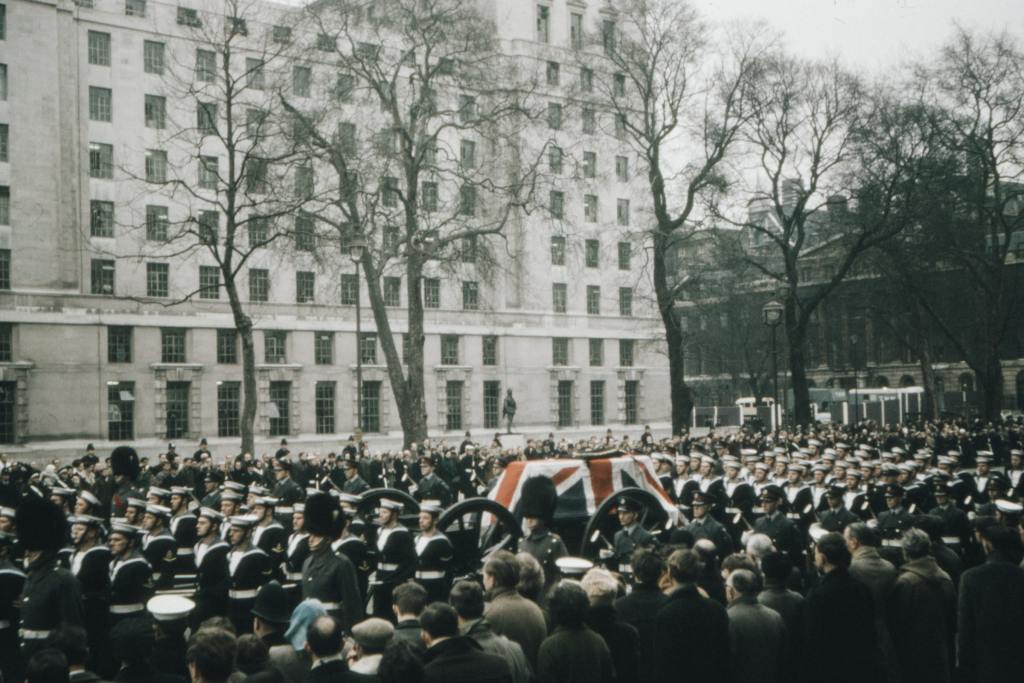 a crowd watching the coffin, that is draped with a union flag, of Winston Churchill pass by in London.