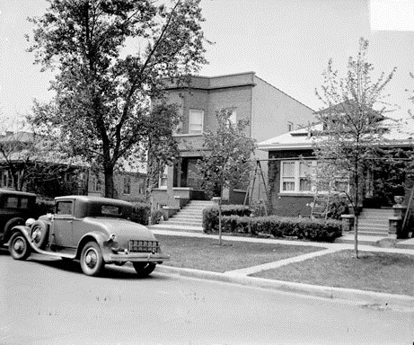 Home of Al Capone, viewed at an angle from across the street, located at 7244 Prairie Avenue in the Greater Grand Crossing community area of Chicago, Illinois. An automobile is parked along the curb in front of the house.