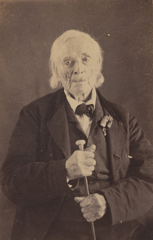 One of the last Veterans of the American Revolutionary War William Hutchings wearing a suit and holding a cane while posing for a photograph.