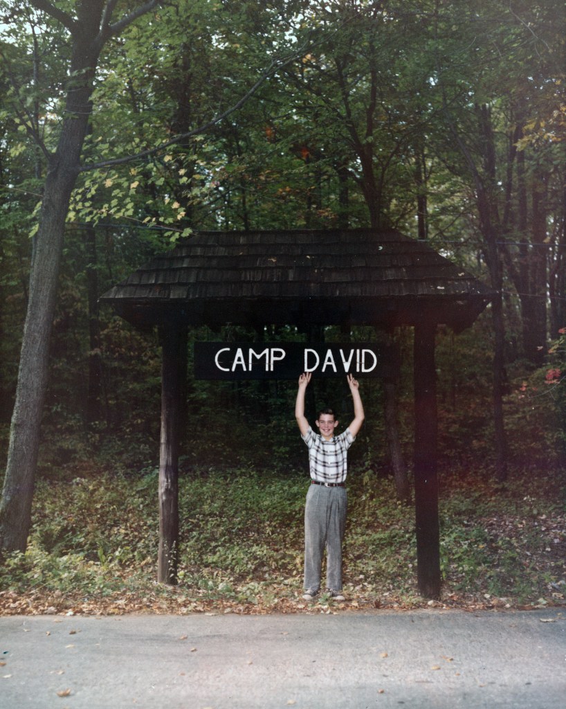 David Eisenhower (age 12), grandson of President Dwight D. Eisenhower, poses with Camp David sign