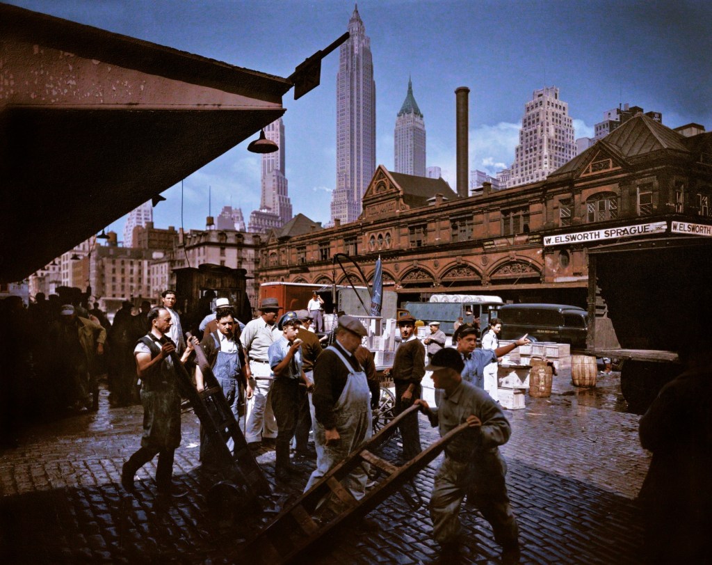 Colorized photograph of the Fulton Street Fish Market, New York City, United States in 1936 showing workers preparing for the day with the New York skyscrapers in the background