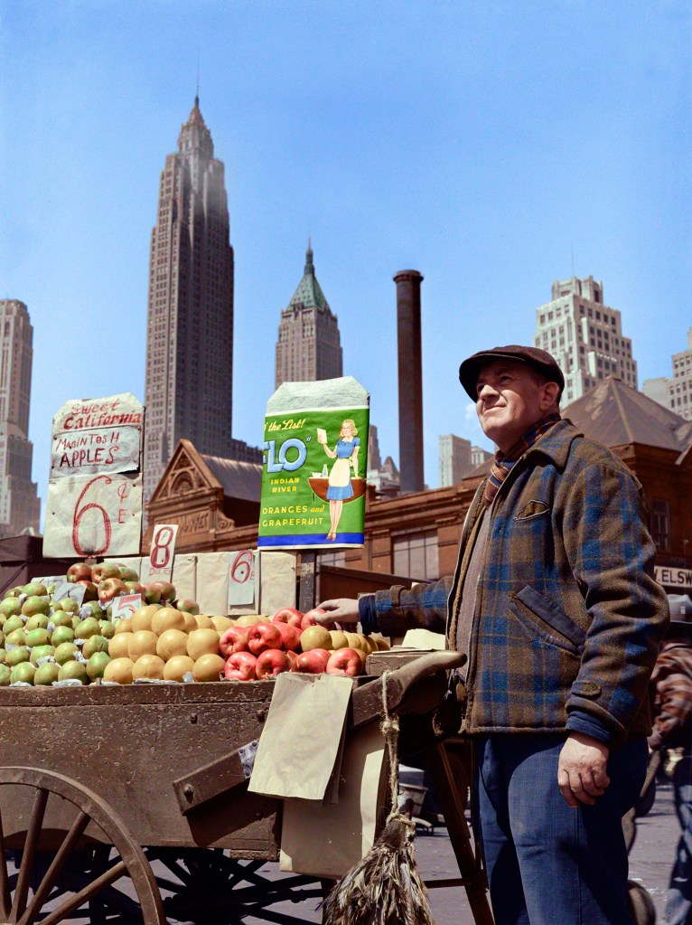 Colorization of A man photographed selling fruits from a pushcart with large buildings of New York in the background