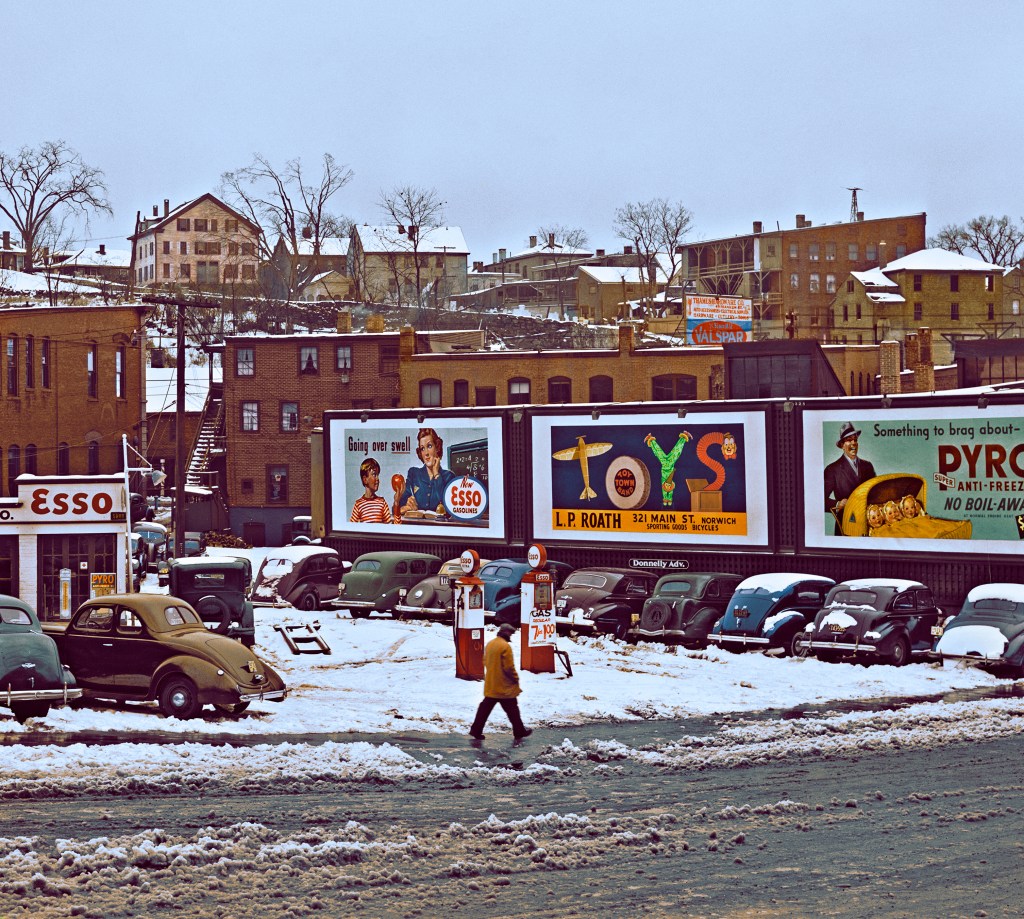 A man walking down a street in Connecticut, United States after a snowstorm. Advertisments are displayed in the background. This image has been colorized