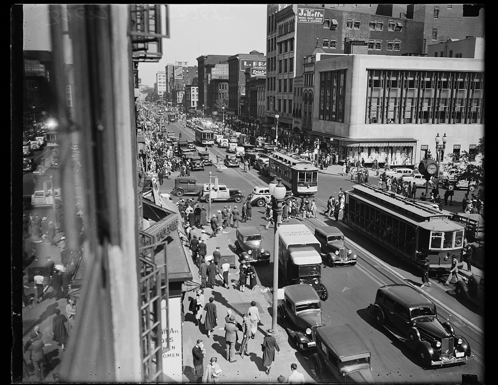 Original black and white photo of a street view of F. Street, N.W., Washington, D.C., United States. Cars, pedestrians and trams fill the street.