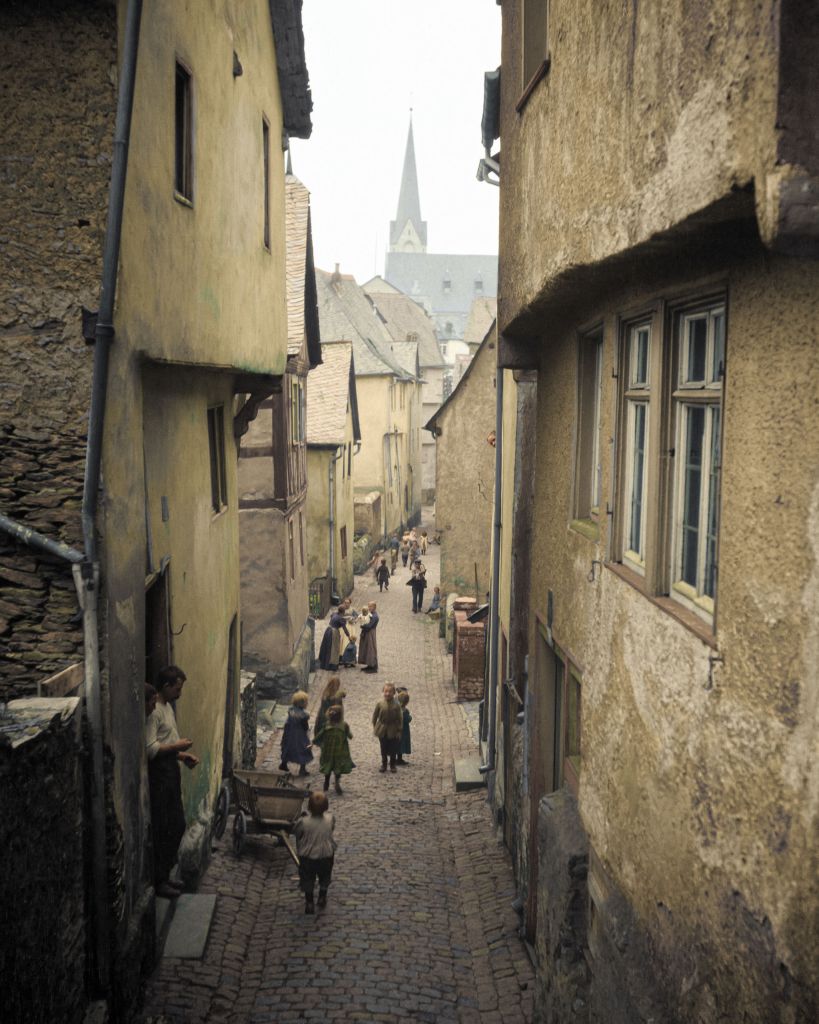 Locals walking on an unidentified narrow street in an unknown European town, likely northern Germany or Belgium. Photograph taken by Arnold Genthe in 1904 during his travels around Europe.