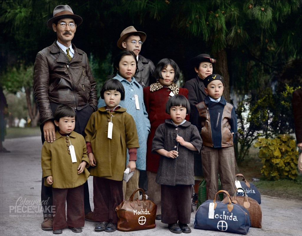Hayward, California. Members of the Mochida family awaiting evacuation bus. Identification tags are used to aid in keeping the family unit intact during all phases of evacuation. Mochida operated a nursery and five greenhouses on a two-acre site in Eden Township. He raised snapdragons and sweet peas. Evacuees of Japanese ancestry will be housed in War Relocation Authority centers for the duration. Image Colorized by Colourised Piece of Jake - World War 2 in Color