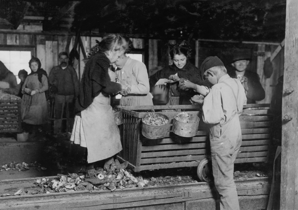 Original Description: Little Nettie [?], a regular oyster-shucker in Alabama Canning Co. She speaks no English. Note the condition of her shoes, caused by standing on the rough shells so much, a common sight. Location: Bayou La Batre, Alabama.