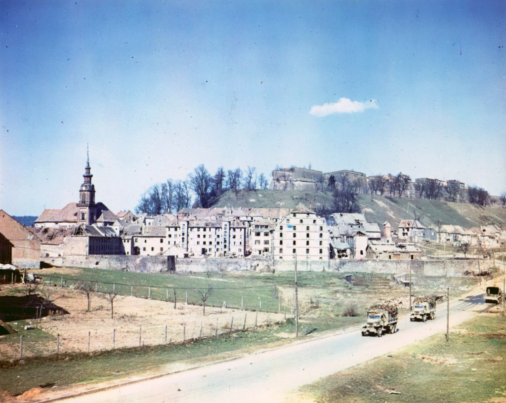 Fort de Bitche in the background and the city of Bitche in the foreground. G.I. trucks carrying P.O.W.s are on the road. 1945.