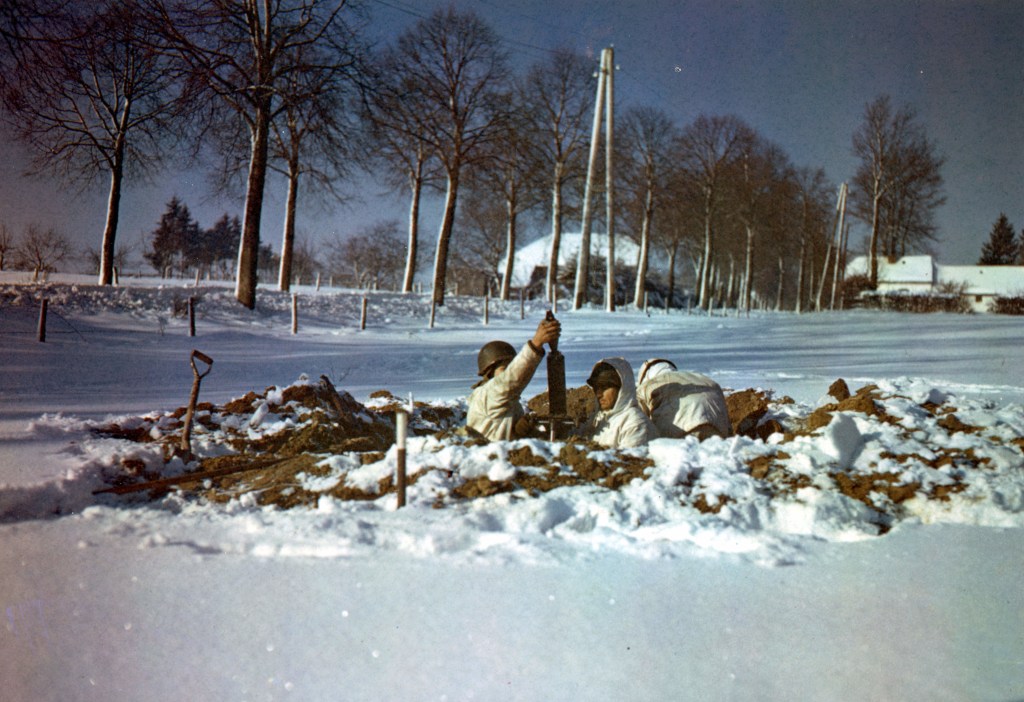 original color photo showing This dug-in mortar emplacement is manned by, left to right, Pvt. R. W. Fierdo, Wyahoga Falls, Ohio; S/Sgt. Adam J. Celinca, Windsor, Conn., T/Sgt. W. O. Thomas, Chicago. St. Vith, Belgium. 24 January, 1945. Photographer: Salis.